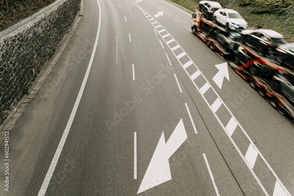 Fototapeta aerial image of a road with an arrow symbol and a truck carrying new cars from the factory , the vehicle is blurred due to movement