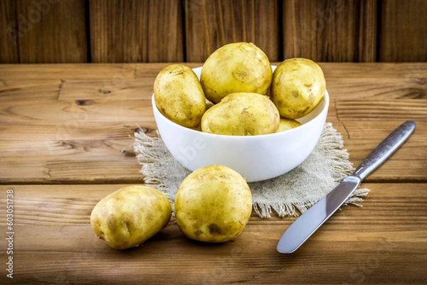 Fototapeta New potatoes with the peel in white plate with knife on wooden background