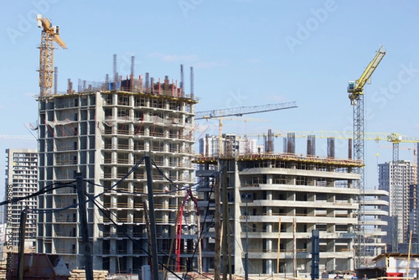 Obraz Construction site. Reinforced concrete frames of multi-storey buildings and construction cranes. Against the background of the blue sky.