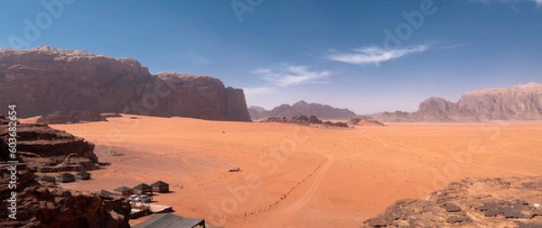 Fototapeta Panorama of Wadi Rum desert with large vast open area of sand and limestone rock formations in the background. Tourist tents visible in the bottom left corner by the rocks.