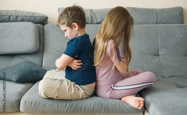 Fototapeta offended brothers and sisters sit back to back on the couch. children's emotions