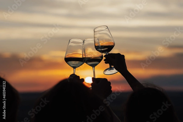 Fototapeta Group of friends with white wine in hands clinking with glasses. Close-up of hands and drinks. Beautiful scenic sunset.	