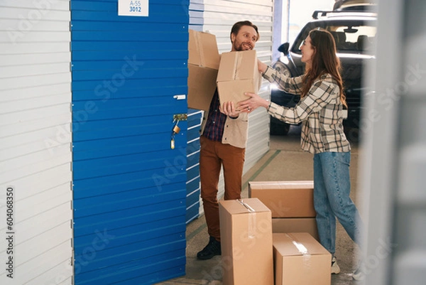 Fototapeta Young couple with big cardboard boxes into warehouse with self storage unit