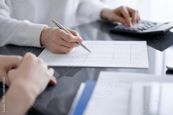 Fototapeta Woman accountant using a calculator and laptop computer while counting taxes for a client. Business audit concepts.
