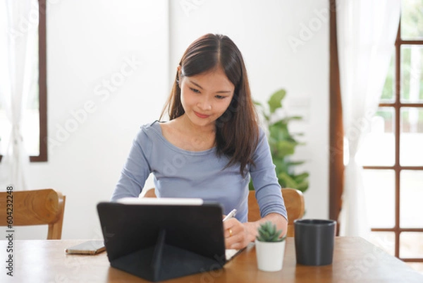 Fototapeta Work from home concept, Business women taking notes while reads data on tablet in living room