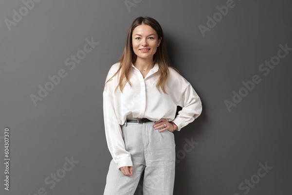 Fototapeta Happy young businesswoman posing isolated over grey wall background. A studio shot of an adult woman standing with a smiling expression