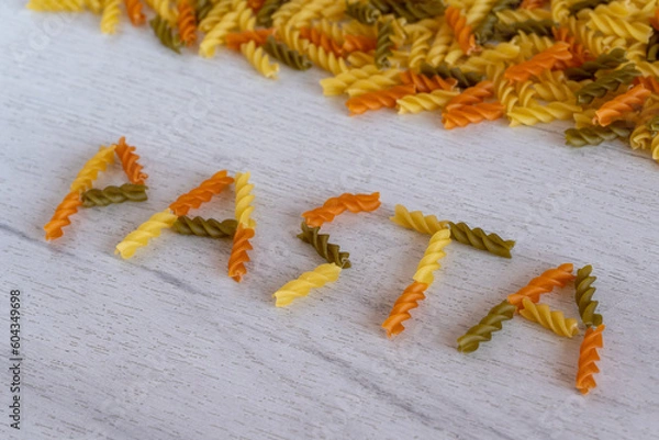 Obraz The word pasta is laid out of fusilli pasta on a white wooden background