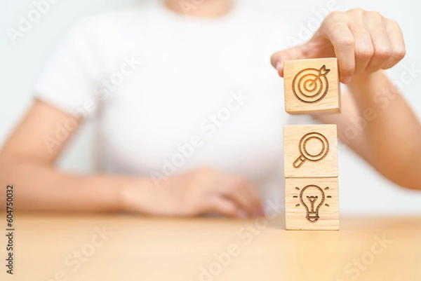 Fototapeta Woman hand holding dartboard above magnifying and Lightbulb icon block. business planning process, goal, vision, strategy, target, mission, action, research, teamwork and idea concept