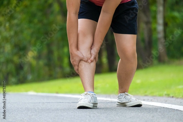Obraz Close-up of young female athlete having knee pain after exercise. Female athlete having leg pain while exercising in park. Exercise injury concept