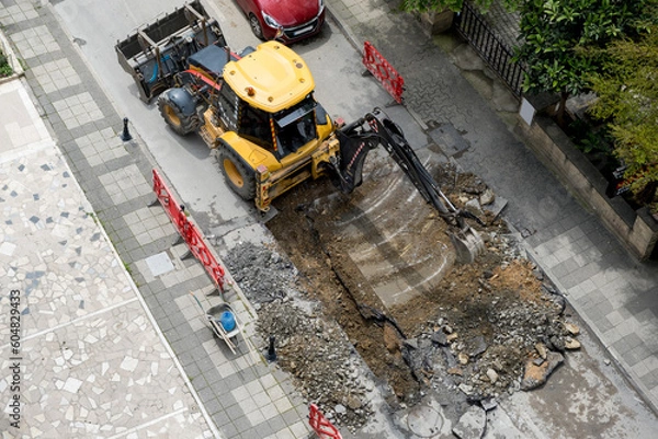 Fototapeta An excavator repairs sewer storm hatches ata street on a summer day. Selective Focus Machine. Top View.