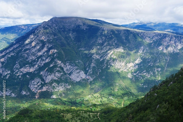 Fototapeta Top view of a small village around the mountain peaks on a sunny day.