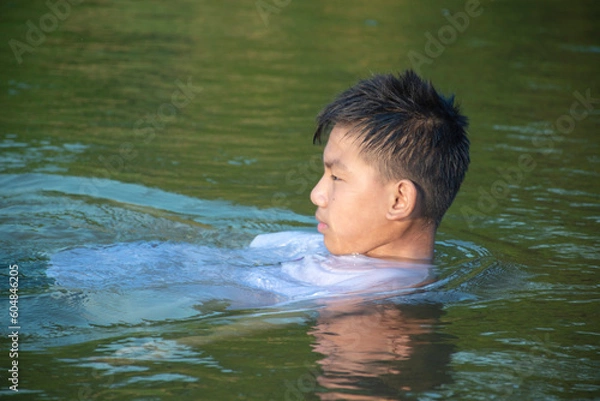 Fototapeta Asian boy in white t-shirt is spending his freetimes by diving, swimming, throwing rocks and catching fish in the river happily, hobby and happiness of children concept, in motion.