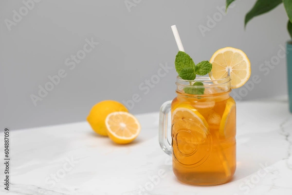 Fototapeta A glass of cold tea, ice cubes, lemon slices and a sprig of mint. Cooling summer drinks.