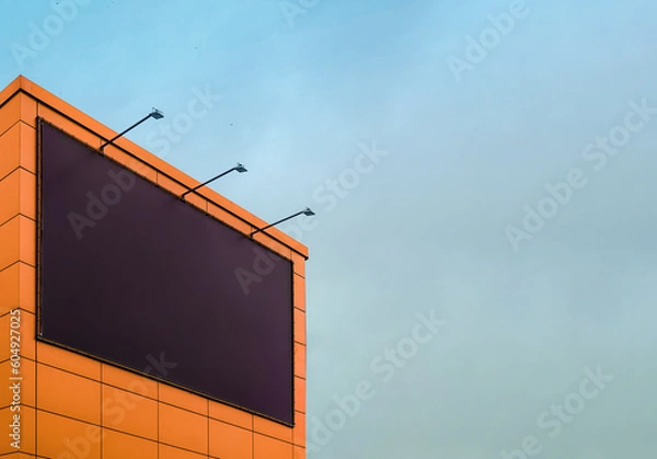Obraz Empty black billboard with backlight on the wall of the building against the sky. Billboard mockup for advertising on the wall of the mall
