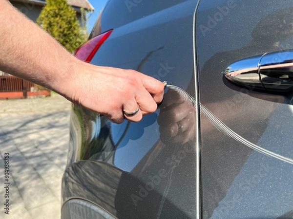 Obraz Man hand scratching a car body surface with a key. Devastation, destroying an expensive car on purpose.