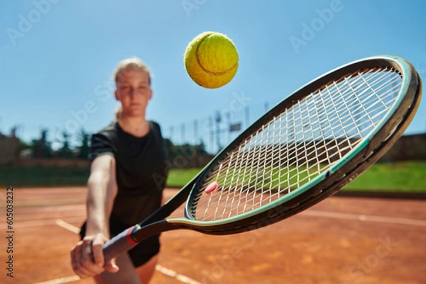Fototapeta Close up photo of a young girl showing professional tennis skills in a competitive match on a sunny day, surrounded by the modern aesthetics of a tennis court.