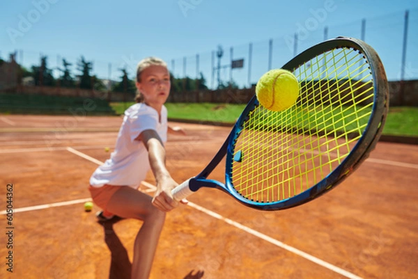 Fototapeta Close up photo of a young girl showing professional tennis skills in a competitive match on a sunny day, surrounded by the modern aesthetics of a tennis court.