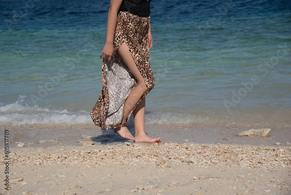 Obraz Young girl walking at the beach in summer vacation. Stylish happy woman wears in leopard pant having fun on the tropical beach with copy space. Close up of legs.