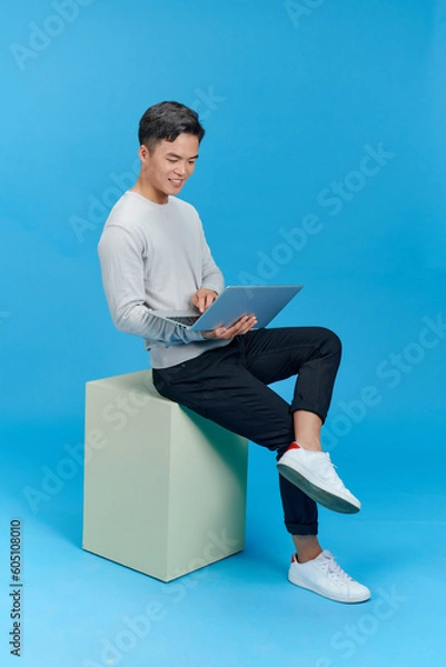 Fototapeta man sitting on a white cube with a laptop computer