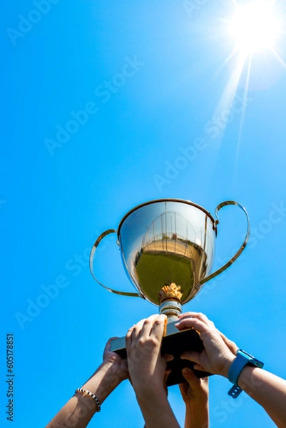 Obraz gold trophy cup in s hands against blue sky background, vertical, winning, school, team success concept 