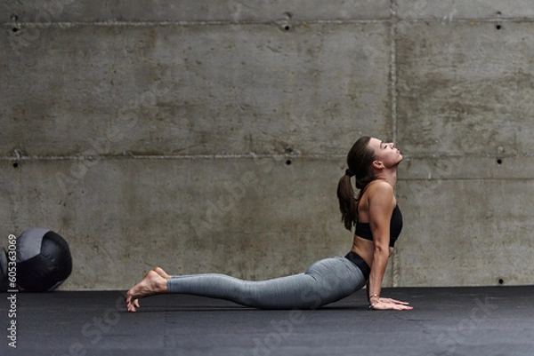 Fototapeta Fit woman in a modern gym working flexibility and strength through various exercises, demonstrating her commitment to fitness