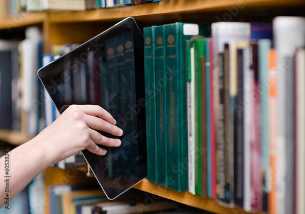 Obraz zbliżenie ręki umieszczenie komputera typu tablet na półkach w bibliotece