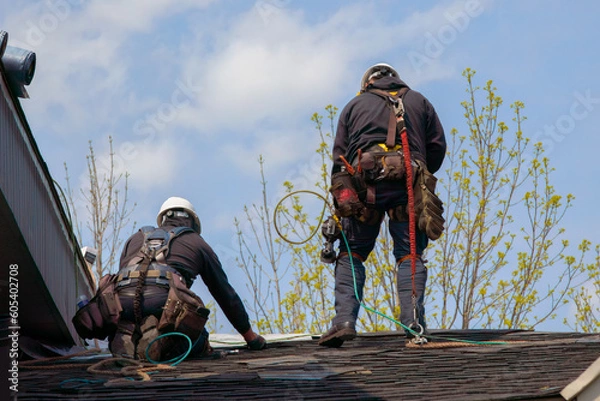 Obraz two mans fixing asphalt shingles working on a roof with security rope