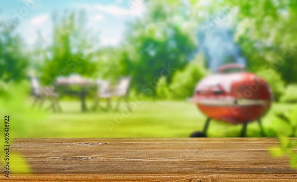 Fototapeta summer time in backyard garden with grill BBQ, wooden table, blurred background