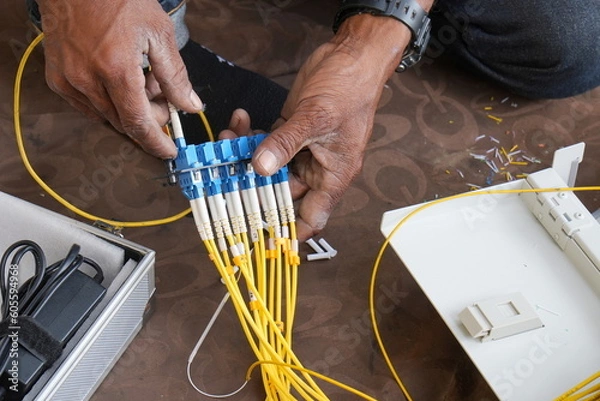 Fototapeta Technician installing fiber optic cable in junction box and testing cables with optical power meter 