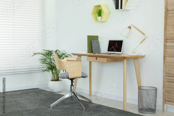 Fototapeta Cozy workspace with modern laptop on desk and comfortable chair at home
