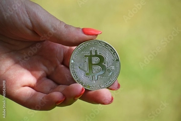 Fototapeta Woman's hand holding a bitcoin against a blurry background.