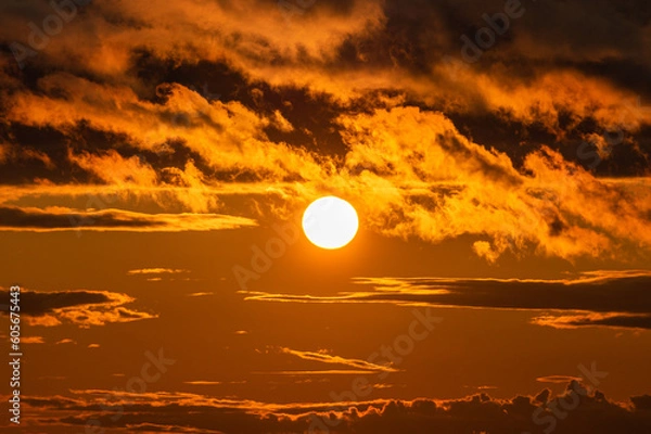Fototapeta The orange setting sun with dramatic clouds.