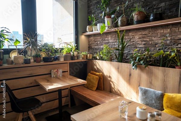 Fototapeta Interior of modern vegan restaurant with many plants as decoration with wooden tables and stone wall.