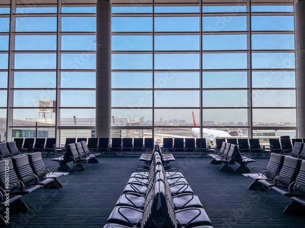 Fototapeta Empty chairs in the departure hall at airport , with the control tower and an airplane taking off at sunset. Travel and transportation concepts.