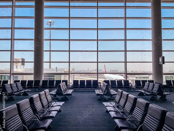 Obraz Empty chairs in the departure hall at airport , with the control tower and an airplane taking off at sunset. Travel and transportation concepts.