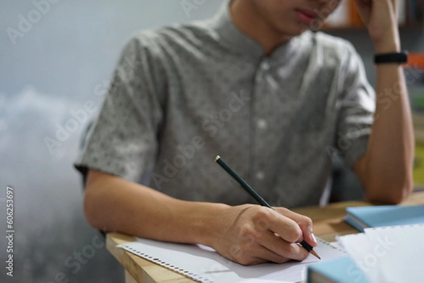 Obraz Man writing on a notebook while studying, working, or take exam