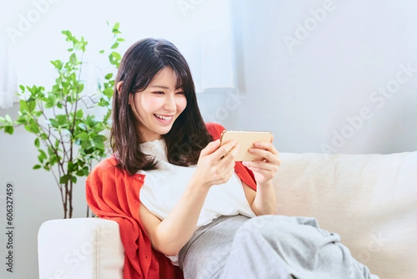 Obraz スマートフォンを横向きにして動画の視聴や鑑賞や電子書籍での読書を楽しむ20代から30代の笑顔の女性