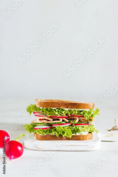 Obraz Delicious and fresh sandwich with greens, ham, cucumber and radish on a wooden board on a light background in the foreground with radish