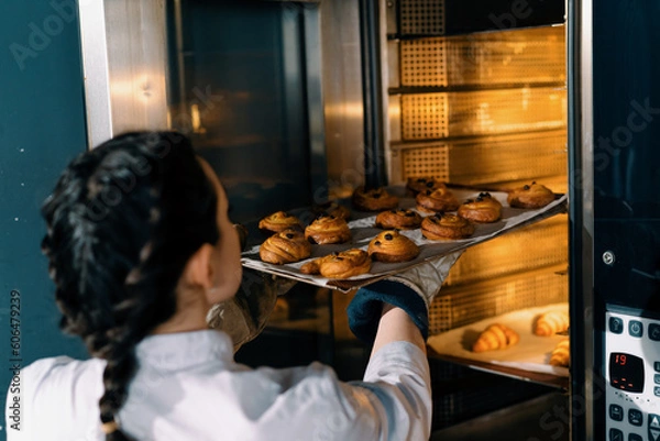 Fototapeta attractive baker takes ready buns and croissants from professional oven bakery production fresh baked goods
