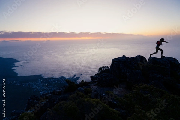 Fototapeta Silhouette of a person in the running in the  mountains having climbed to the top of a mountain at sunrise