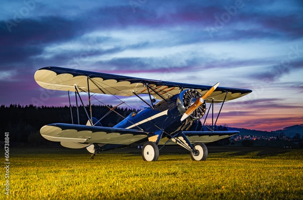 Fototapeta Parked vintage bi-plane photographed during sunset. This plane has a radial engine and an open cockpit. The colorful sky makes this foto a beautiful aviation wallpaper