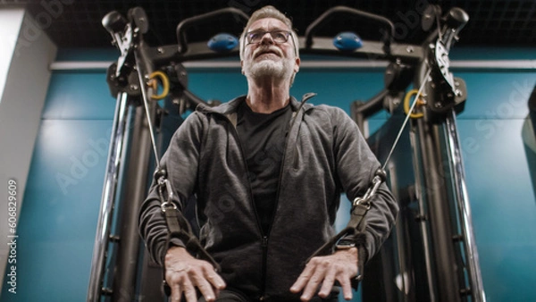 Fototapeta Senior active male in his 60s working out on a pulley machine in the gym