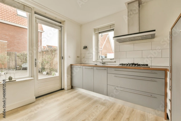 Fototapeta a kitchen with wood flooring and white tile on the walls, in front of an open window looking out onto a brick wall
