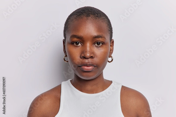 Fototapeta Portrait of young A American woman confidently looks at camera stands indoor dressed in comfortable tshirt has simple expression reveals depth of thought and contemplation poses over white background