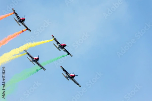 Fototapeta Airplanes squadron in arrow formation doing tricks and stunts over the blue sky with color wakes on a summer day at Gijon air show festival