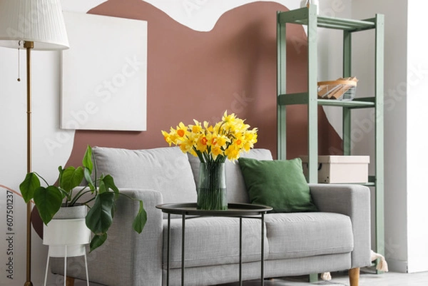 Fototapeta Interior of stylish living room with cozy grey sofa and blooming narcissus flowers on coffee table