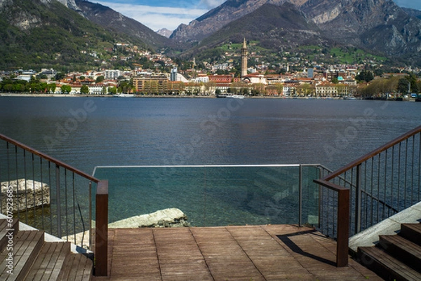 Fototapeta Buildings of the city of Lecco on the shores of Lake Como surrounded by mountains in the background. View from the promenade in Malgrate