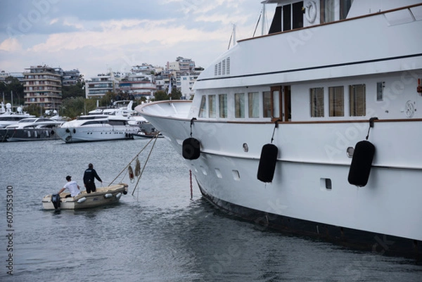 Fototapeta Big white yacht in marina and port staff men on a small boat 