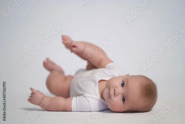Fototapeta A newborn baby is trying to roll over on his stomach. photography on a light background