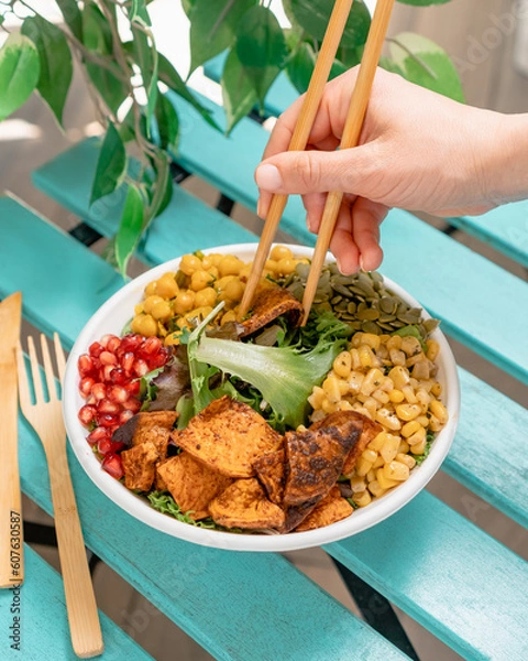 Fototapeta Salad bowl in disposable plate with fresh greens, pomegranate, chickpeas, seeds and seaweeds eating with chopsticks. 